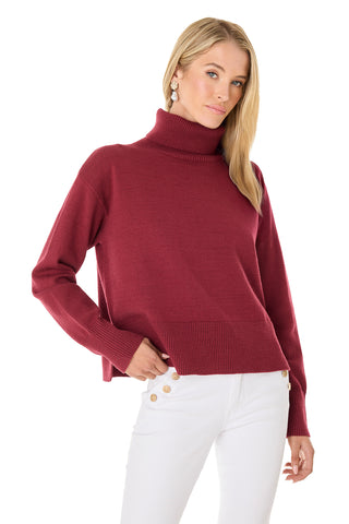 A woman with long blonde hair wears the Gia Ultra Soft Sweater in Merlot and white buttoned pants, posing against a white background.