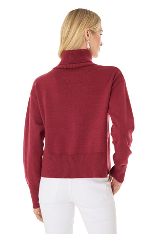A woman with blonde hair is seen from the back, wearing the Gia Ultra Soft Sweater in Merlot and white pants. She stands with one hand in her pocket against a white background.