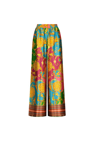 The Marcia Silk Pant - Dolce Sun features a baroque-style summer print in yellow, green, pink, and blue on white silk. These designer pants have wide legs, an elastic waistband, and ornate decorative motifs.