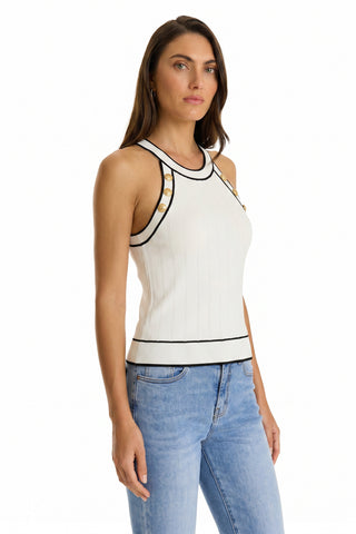 A woman with long brown hair wears the Martha Button Halter Tank in white—a sleeveless ribbed top with black trim and gold shoulder buttons—paired with light blue jeans, standing against a plain white background.