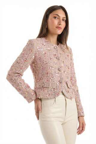 A woman wears the May Tweed Crystal Jacket in Pink Multi, featuring sequined florals and structured shoulder pads, paired with light high-waisted pants. She confidently looks at the camera against a white background.