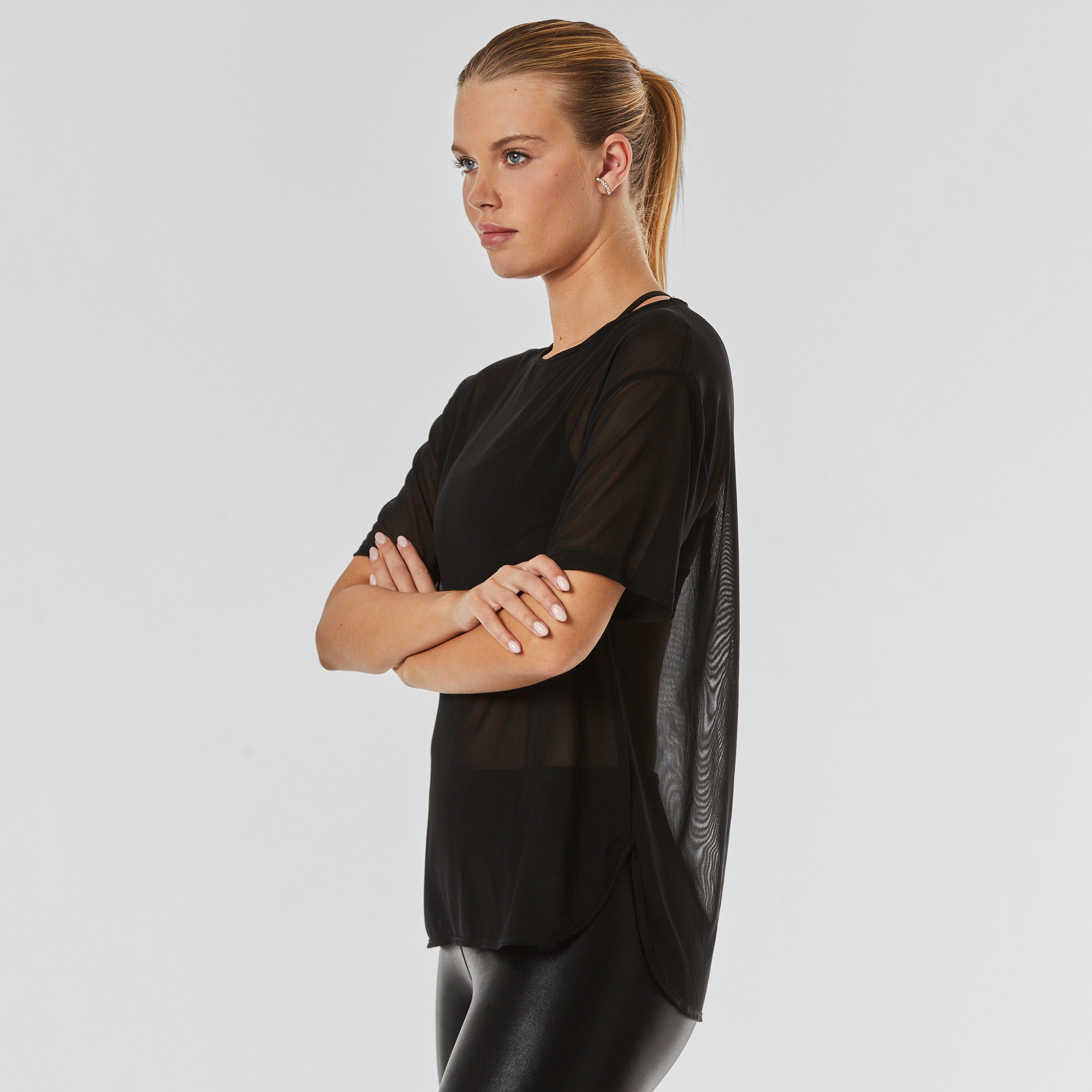 Side view of woman wearing ultra-stretchy and silky soft black mesh shirt, featuring short sleeves and classic neckline