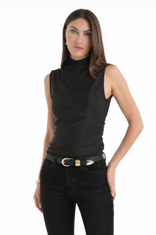 A woman with straight brown hair wears the Mia Shimmer Tank - Black, paired with black jeans and a gold-buckled belt, standing with one hand in her pocket against a white background.
