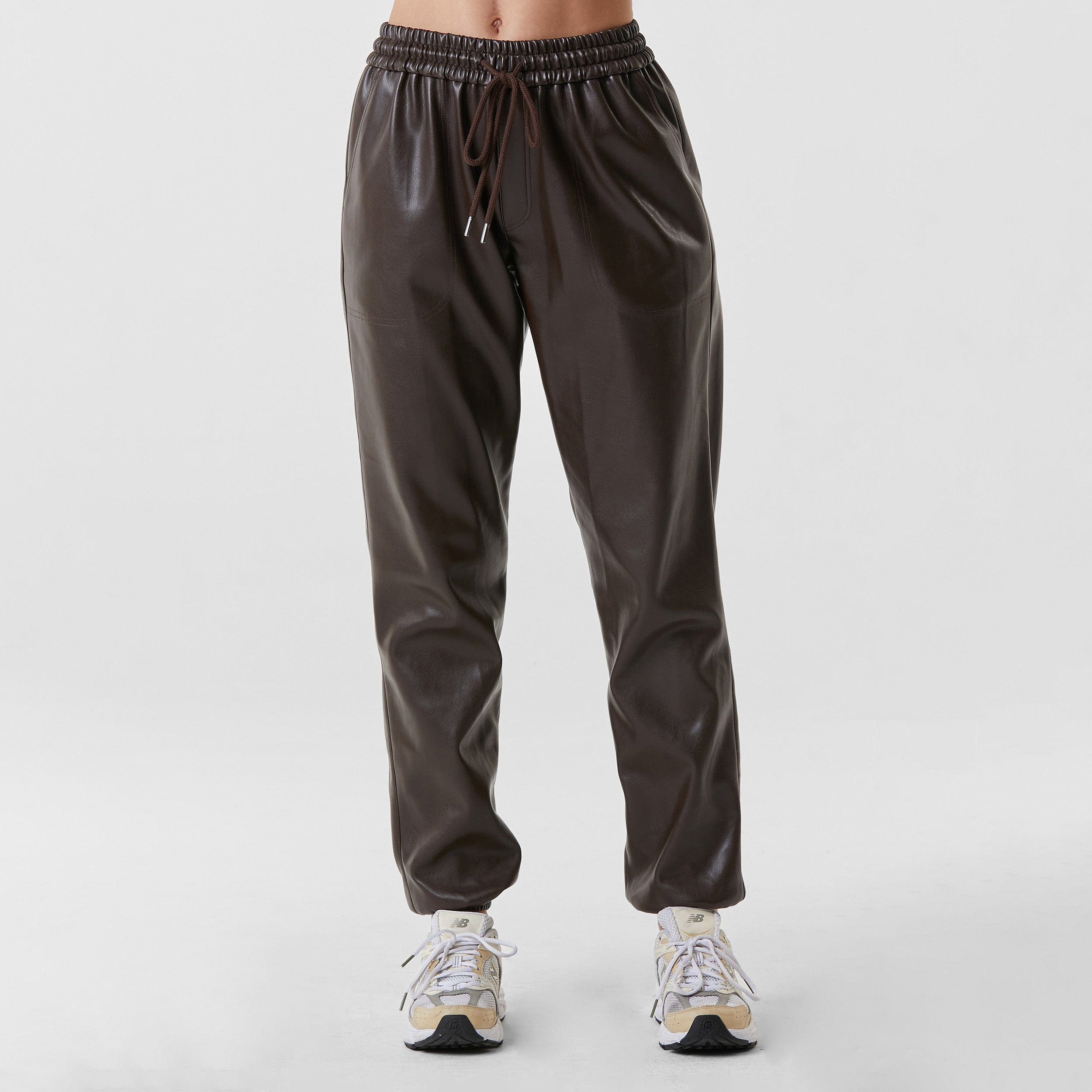 Front view of woman wearing dark brown high rise faux leather jogger with drawstring waistband and cinched ankles with suede lining.