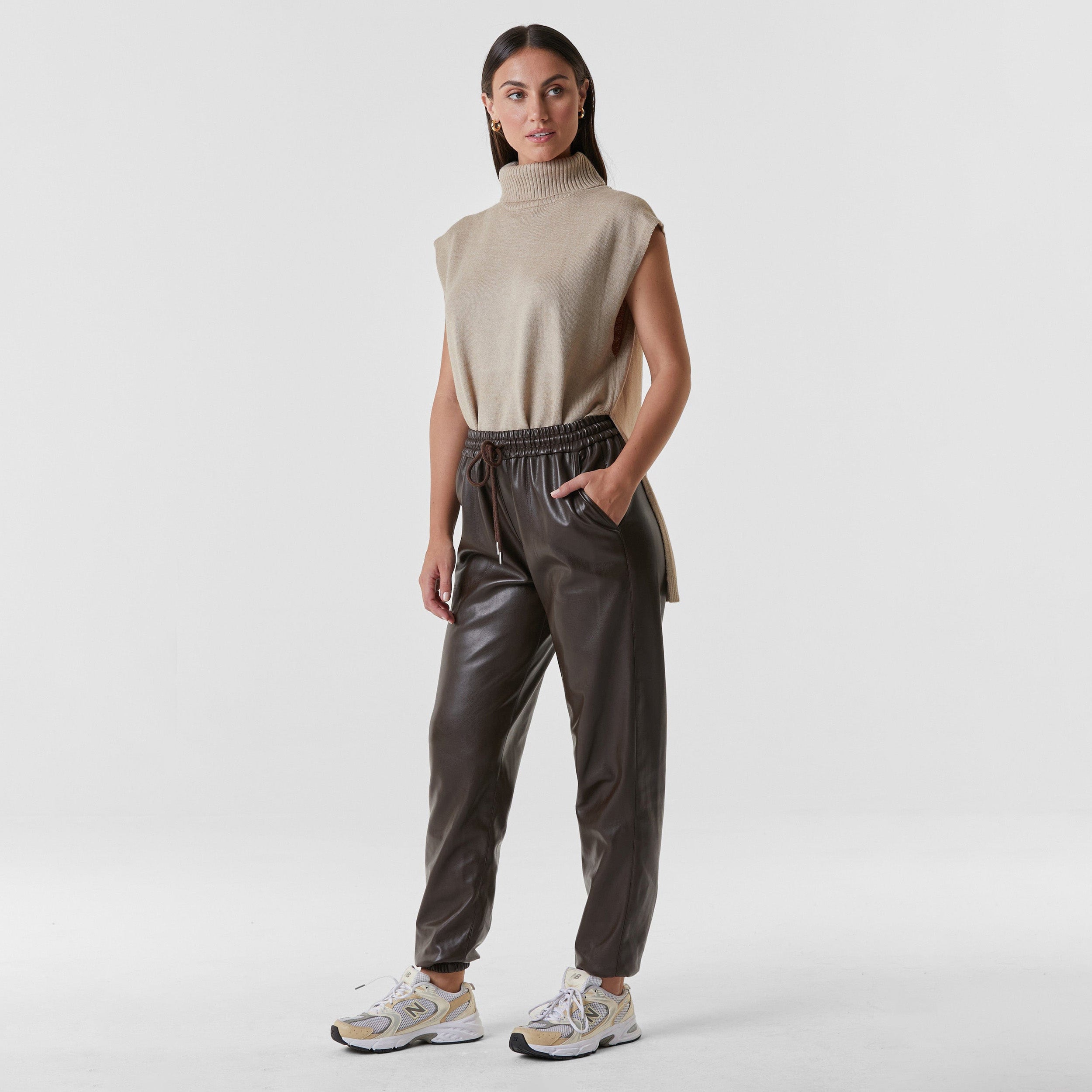 Full view of woman wearing dark brown high rise faux leather jogger with drawstring waistband and cinched ankles with suede lining.
