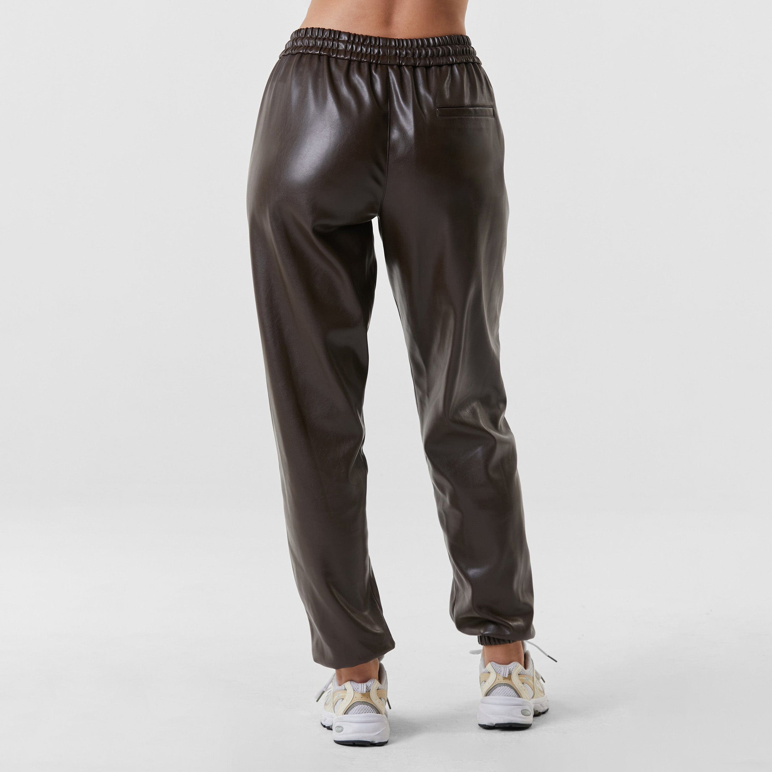 Rear view of woman wearing dark brown high rise faux leather jogger with drawstring waistband and cinched ankles with suede lining.