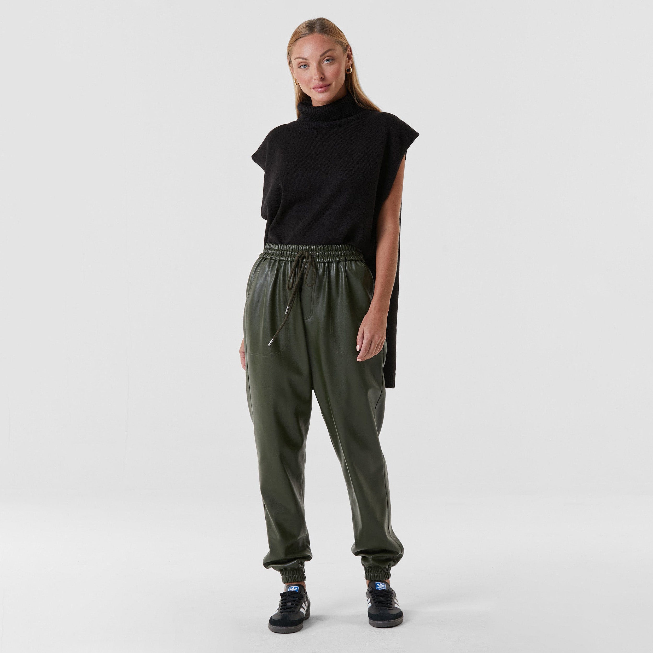 Full body view of woman wearing hunter green high rise faux leather jogger with drawstring waistband and cinched ankles with suede lining.