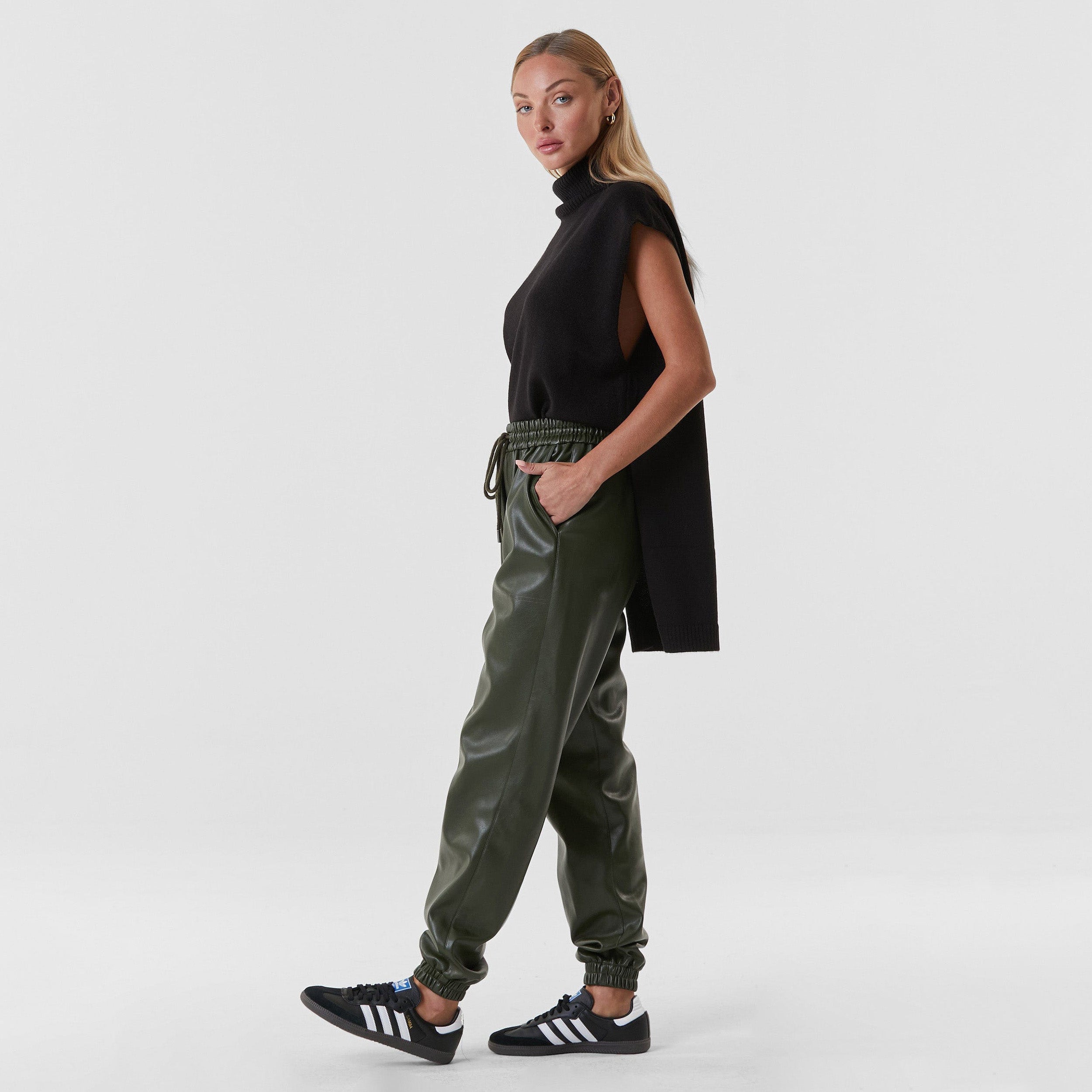 Side view of woman wearing hunter green high rise faux leather jogger with drawstring waistband and cinched ankles with suede lining.
