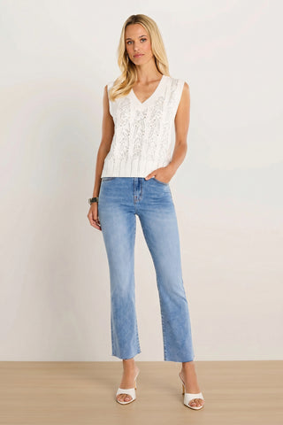 A woman with long blonde hair stands confidently against a plain background wearing the Mikaela Crystal Knit Top in white, light blue jeans, white heeled sandals, and a bracelet.