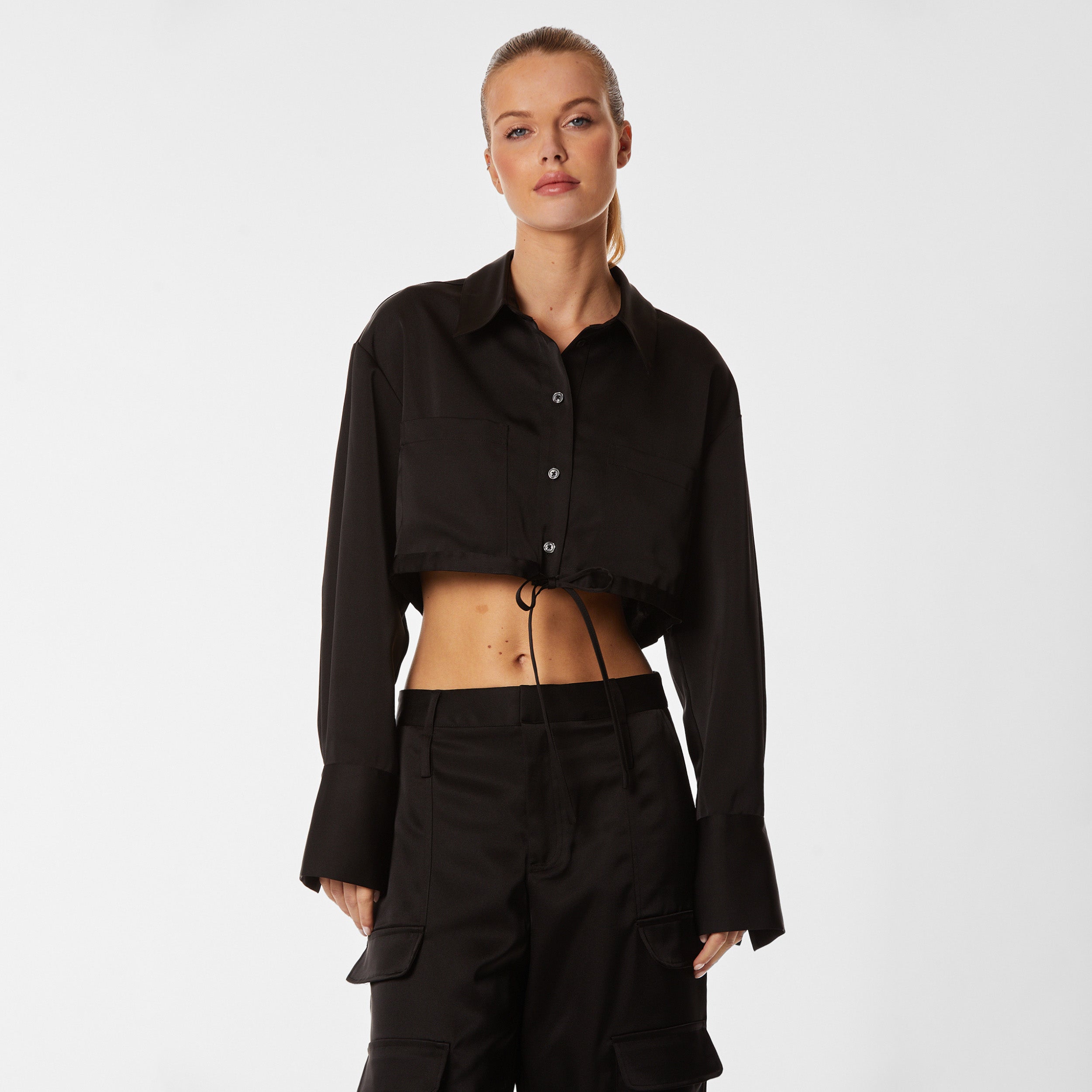 Front view of woman wearing black Milan Satin Button Up features luxurious and structured satin-like fabric, featuring cargo detailing, shell buttons and a tie-waist