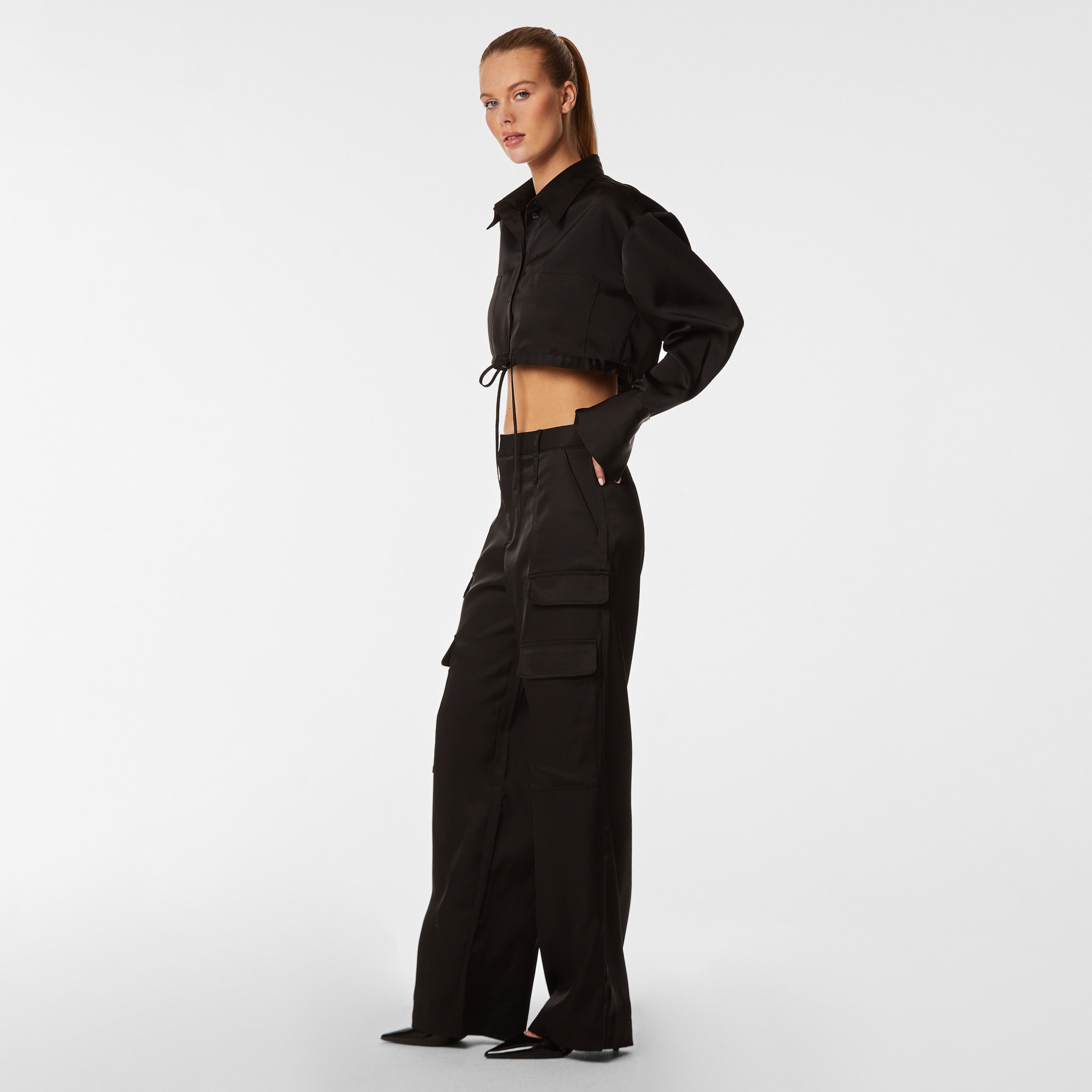 Side view of woman wearing black Milan Satin Button Up features luxurious and structured satin-like fabric, featuring cargo detailing, shell buttons and a tie-waist