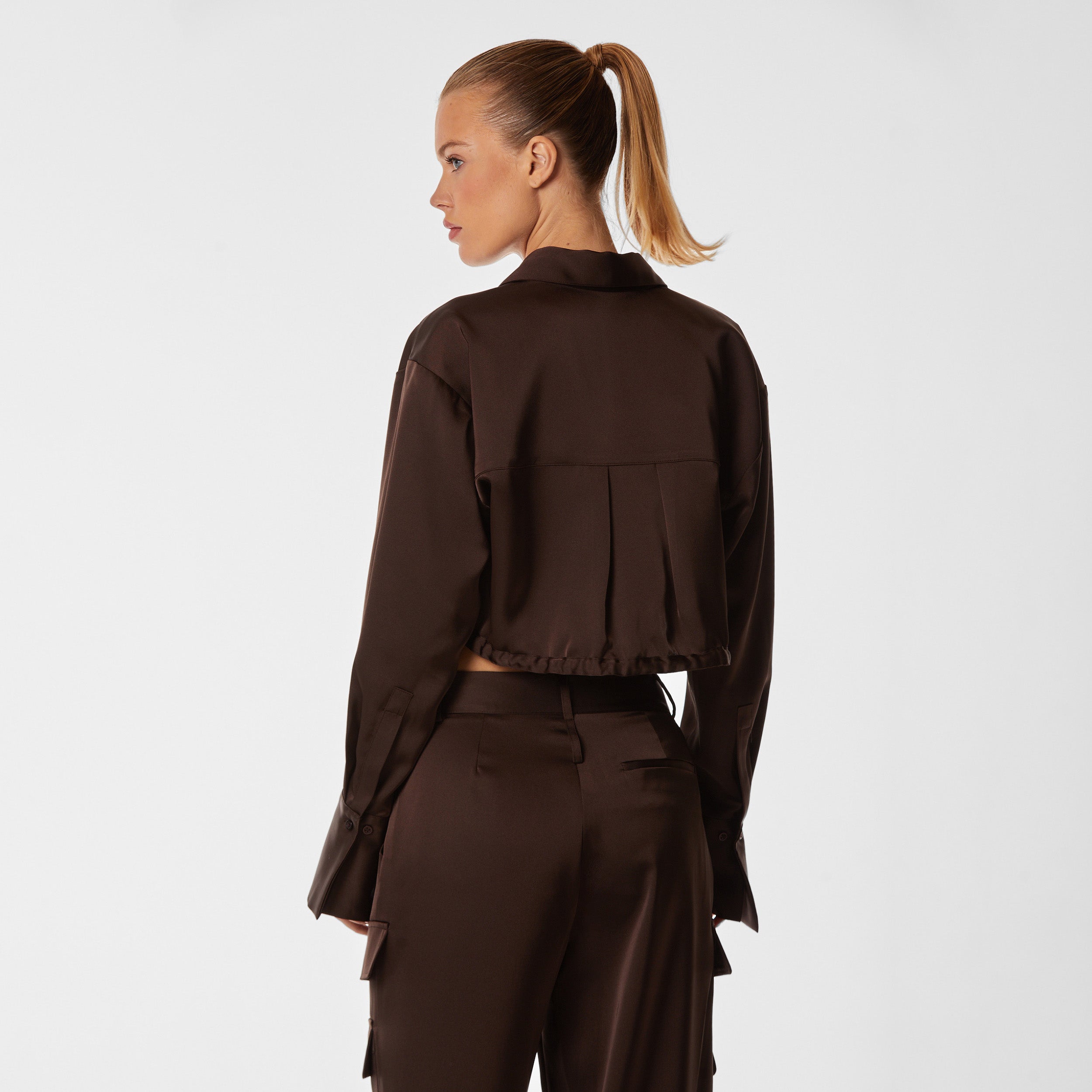 Rear view of woman wearing brown Milan Satin Button Up features luxurious and structured satin-like fabric, featuring cargo detailing, shell buttons and a tie-waist