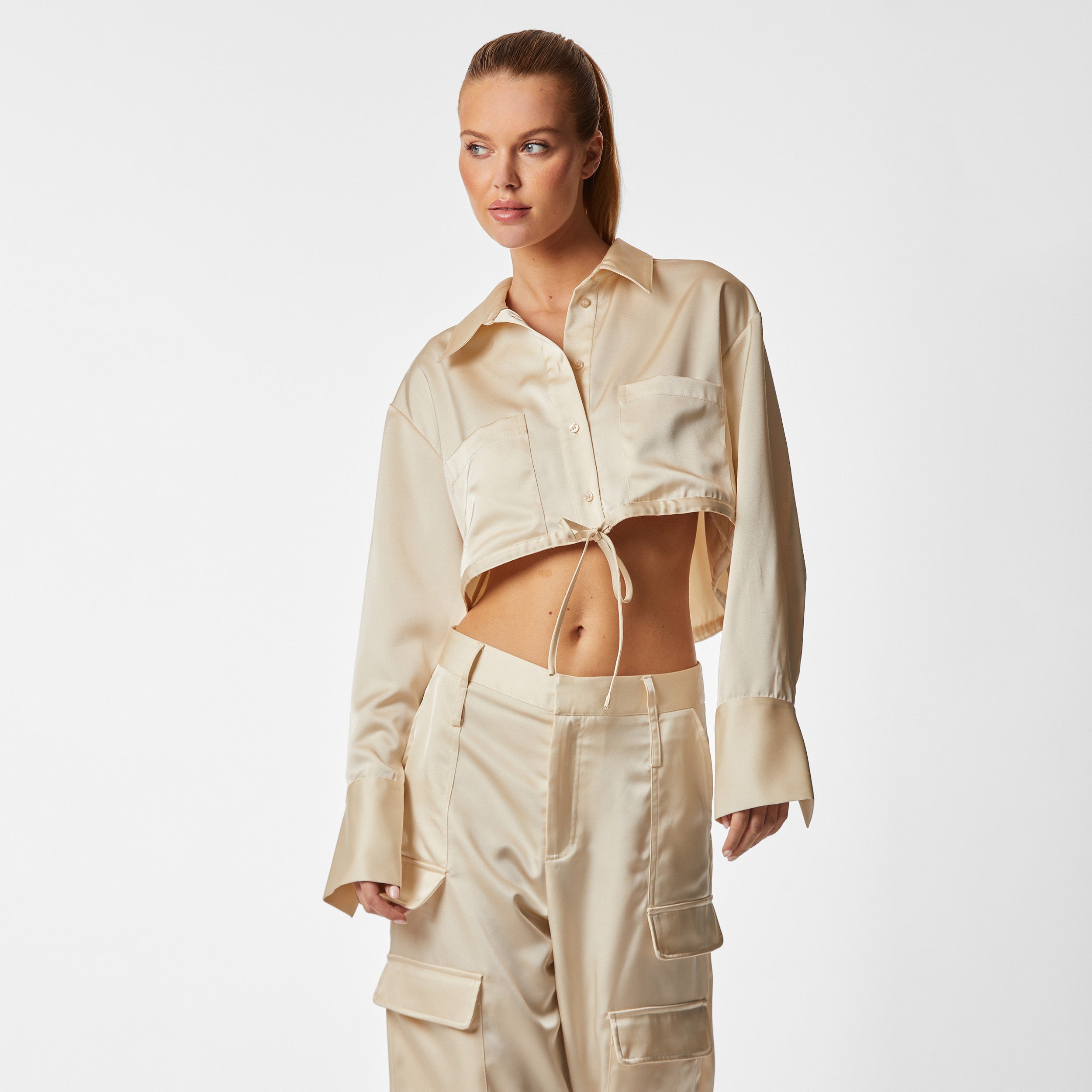 Front view of woman wearing pearl Milan Satin Button Up features luxurious and structured satin-like fabric, featuring cargo detailing, shell buttons and a tie-waist
