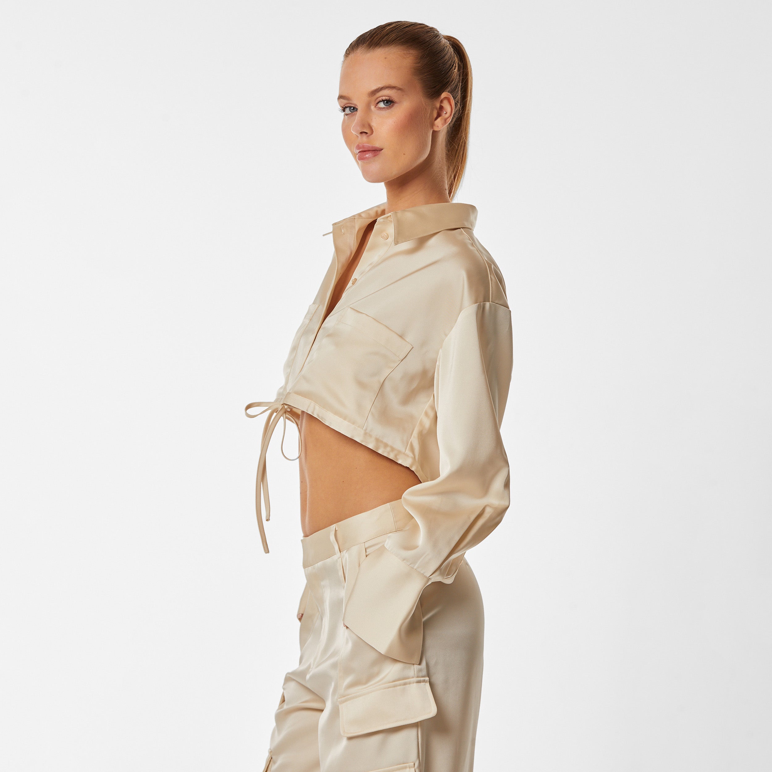 Side view of woman wearing pearl Milan Satin Button Up features luxurious and structured satin-like fabric, featuring cargo detailing, shell buttons and a tie-waist