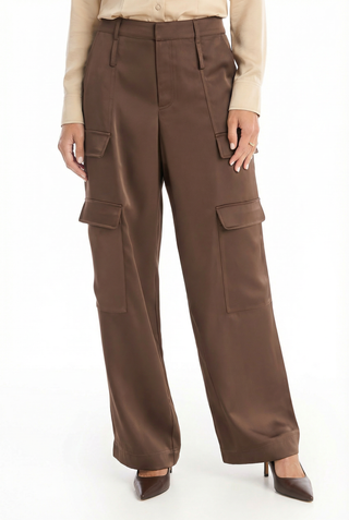 Someone wearing the Milan Satin Cargo Pant in Espresso, featuring wide legs and large side pockets, paired with a beige long-sleeve shirt and brown pointed-toe heels, stands against a white background.
