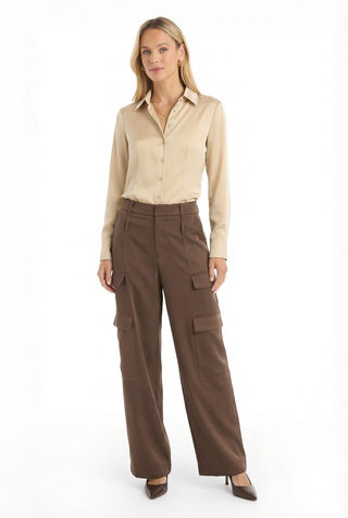 A woman stands against a white background wearing the Milan Satin Cargo Pant in Espresso, featuring large pockets and a satin-like finish, paired with a beige shirt and brown heels for a relaxed, confident look.