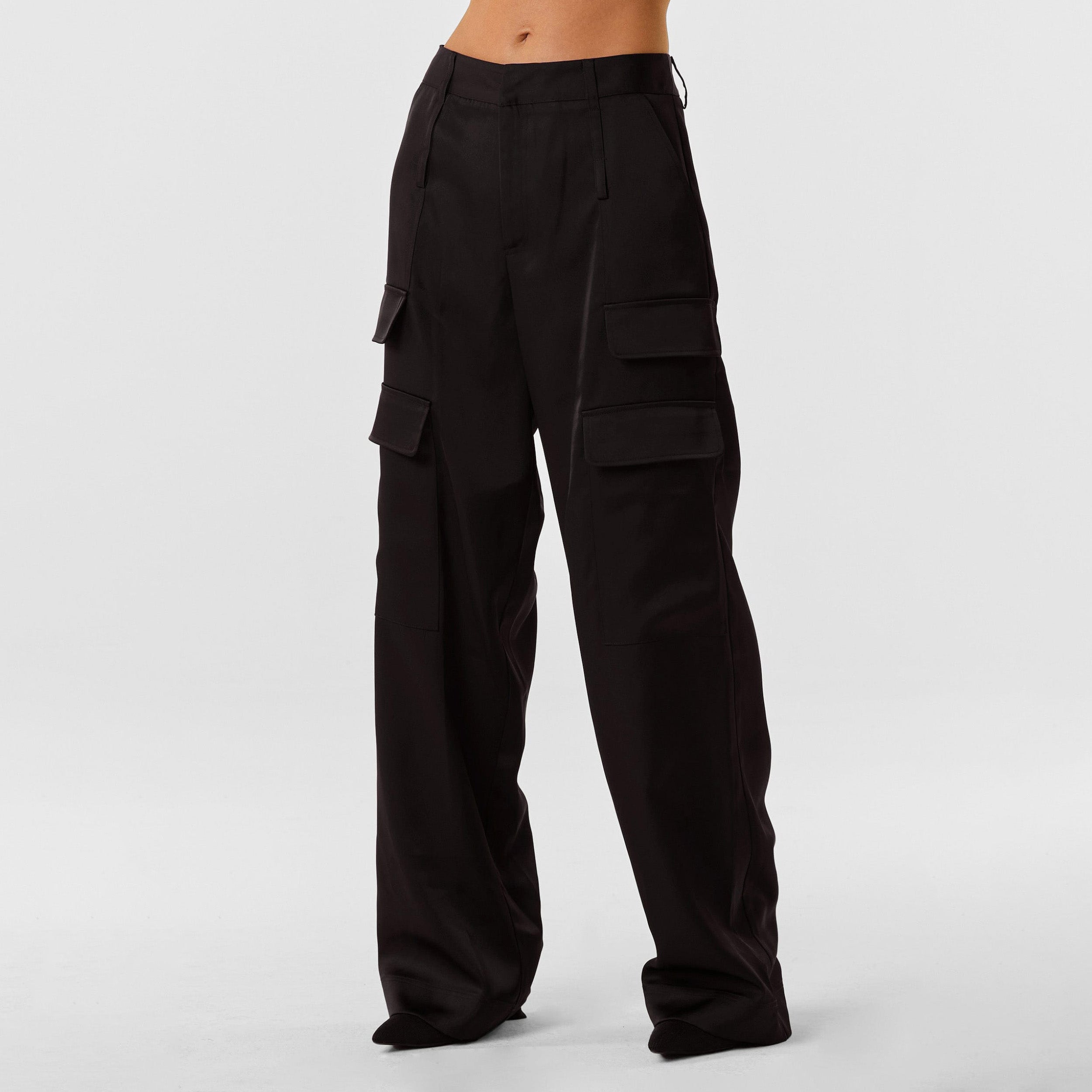Front view of woman wearing Black Satin Milan Pant features Mid-rise with side pockets and cargo detail. Luxurious and structured satin-like fabric. 
