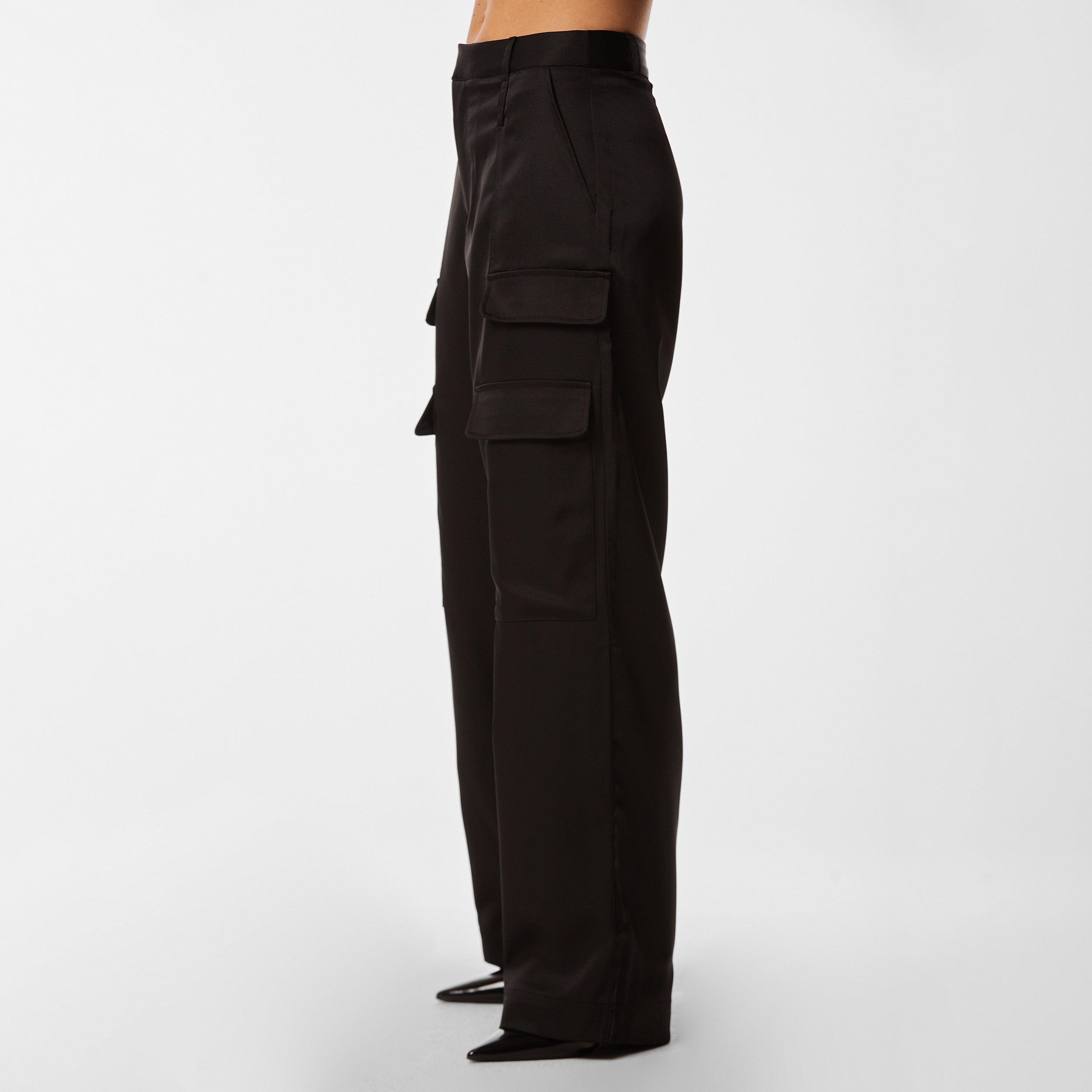 Side view of woman wearing Black Satin Milan Pant features Mid-rise with side pockets and cargo detail. Luxurious and structured satin-like fabric. 