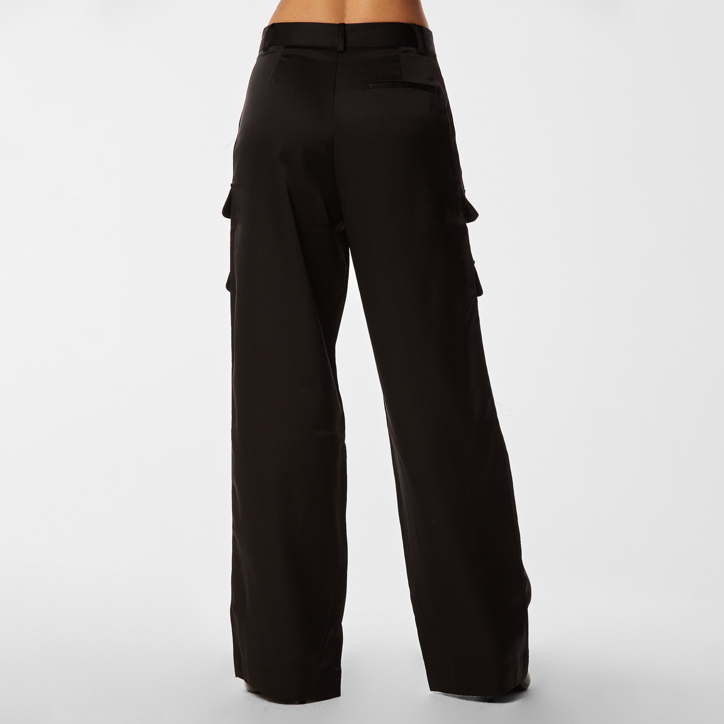 Rear view of woman wearing Black Satin Milan Pant features Mid-rise with side pockets and cargo detail. Luxurious and structured satin-like fabric. 