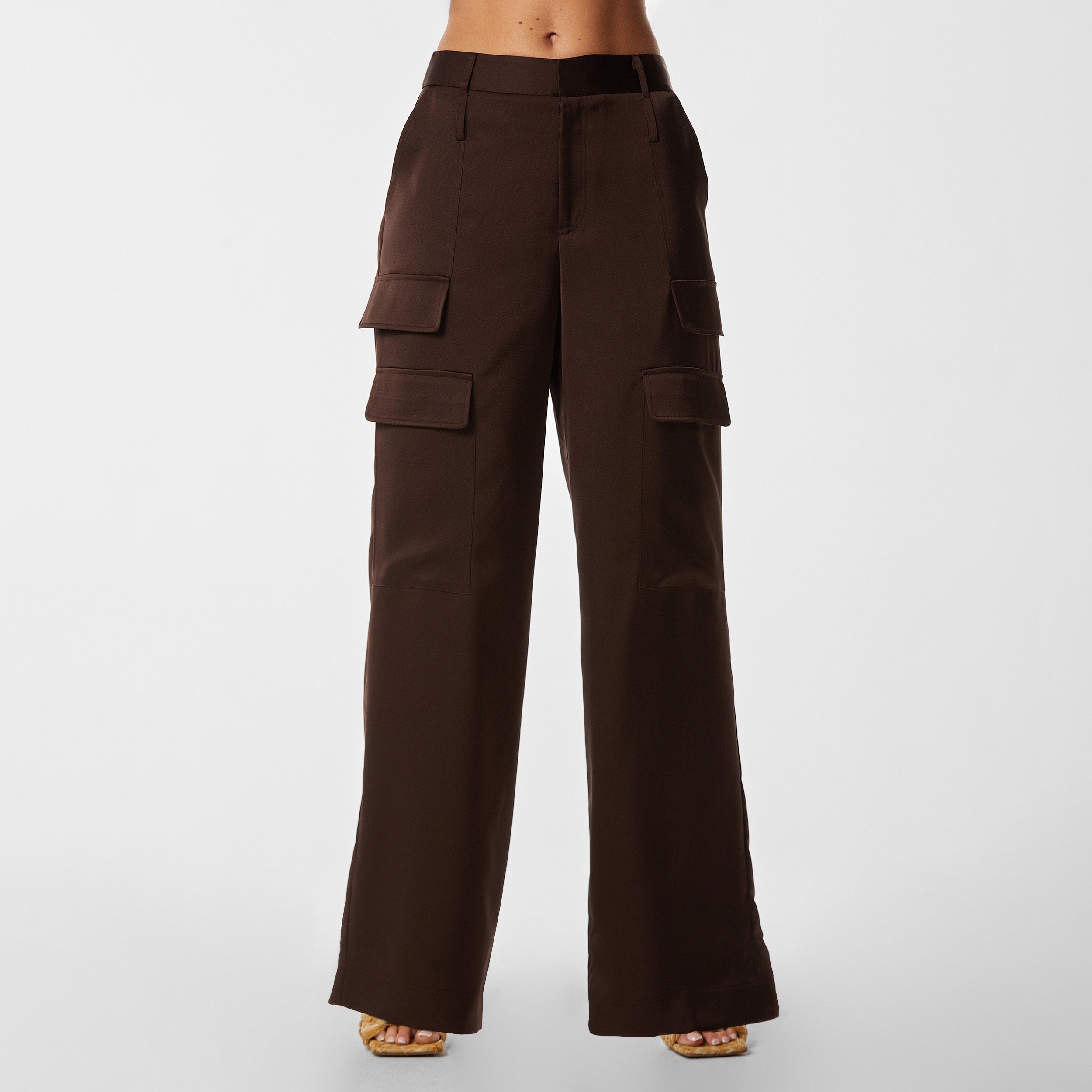 Front view of woman wearing Brown Satin Milan Pant features Mid-rise with side pockets and cargo detail. Luxurious and structured satin-like fabric. 