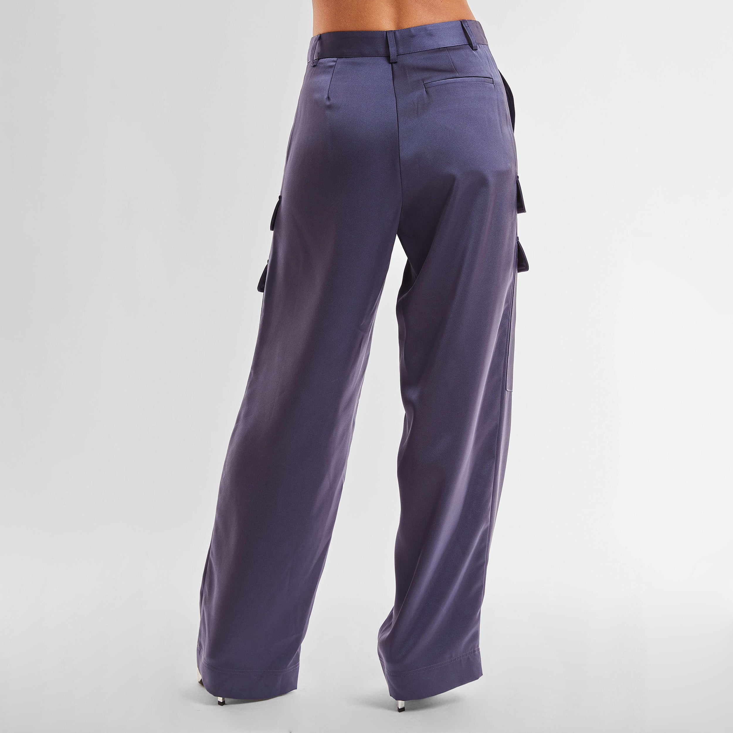 Rear view of woman wearing Navy Satin Milan Pant features Mid-rise with side pockets and cargo detail. Luxurious and structured satin-like fabric. 