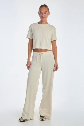 Against a white background, a person wears the Daphne Soft T-Shirt in Pearl, a light beige short-sleeve crop top paired with matching wide-leg pants. This ultra-soft casual outfit, completed with sneakers, is an essential wardrobe staple.