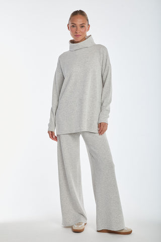 A person stands in a relaxed pose wearing the loose-fitting Daphne Top in Heather Grey paired with matching wide-leg pants. Made from a soft modal blend, this outfit provides luxurious comfort and resembles cozy loungewear. The background is plain white.