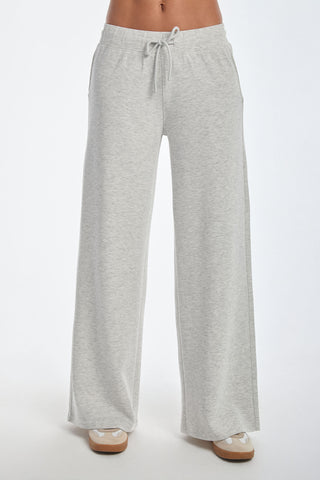 The Daphne Pant - Heather Grey, made from a soft modal blend, features a wide-leg design and adjustable drawstring waist for luxurious comfort. Paired with beige sneakers, this sophisticated look is enhanced by convenient side pockets against a plain white backdrop.