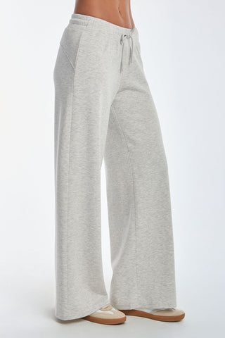 A person in Daphne Pant - Heather Grey, featuring a luxurious soft modal blend and wide-leg design with a waist drawstring, pairs them with tan sneakers against a plain white background.