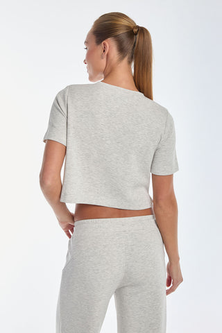 A person with a ponytail wears the Daphne Soft T-Shirt in Heather Grey, paired with matching pants, showcasing its ultra-soft fabric from behind against a plain white backdrop.