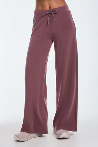 Embrace luxurious comfort in the Daphne Pant - Orchid, featuring high-waisted, wide-leg design and an adjustable drawstring. Crafted from a smooth modal blend and paired with light sneakers against a white background, this ensemble is perfect for travel adventures.