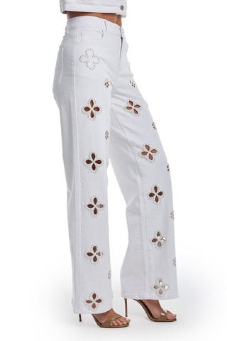 A person is shown from the waist down wearing the Kaia Pearl High Rise Jean in white with floral cut-outs, paired with beige high-heeled sandals.