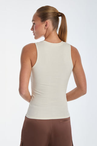A person with their hair in a ponytail wears a fitted, sleeveless Rosette Tank Top - Pearl and brown pants, standing slightly turned away from the camera against a plain background.