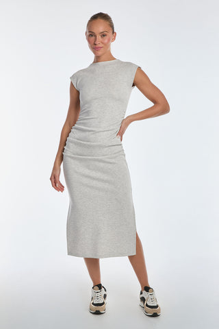 A person confidently poses with one hand on their hip, wearing a fitted sleeveless Daphne Dress in Heather Grey. The ultra-soft heathered modal fabric pairs perfectly with their black and white sneakers as they smile against a plain white backdrop.