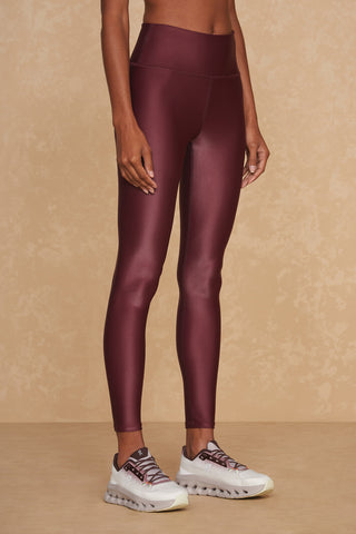 A person wearing Liquid Legging - Cherry and white athletic shoes stands against a beige textured background. Their upper body is not visible, but the squat-proof assurance of the Xtra Life Lycra fabric promises immaculate style and comfort.