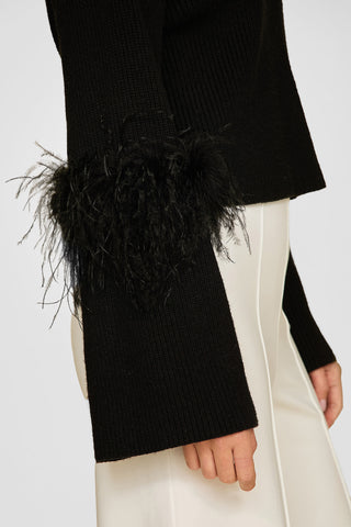 Dressed in the elegant Bella Feather Trim Sweater - Black, featuring a ribbed design with feathered cuffs, paired with white pants, one can't help but notice the exquisite sleeve detailing.
