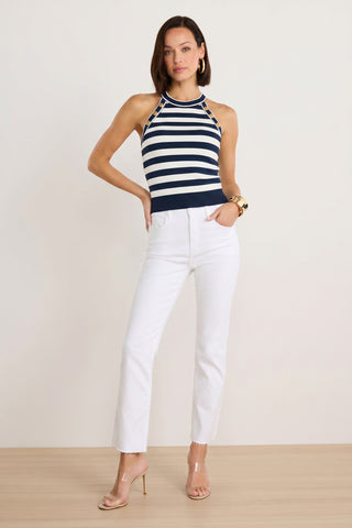 A woman poses against a plain background in the Martha Button Halter Tank - Navy Stripe, paired with white high-waisted jeans, nude heels, and gold jewelry for a chic, nautical-inspired look.