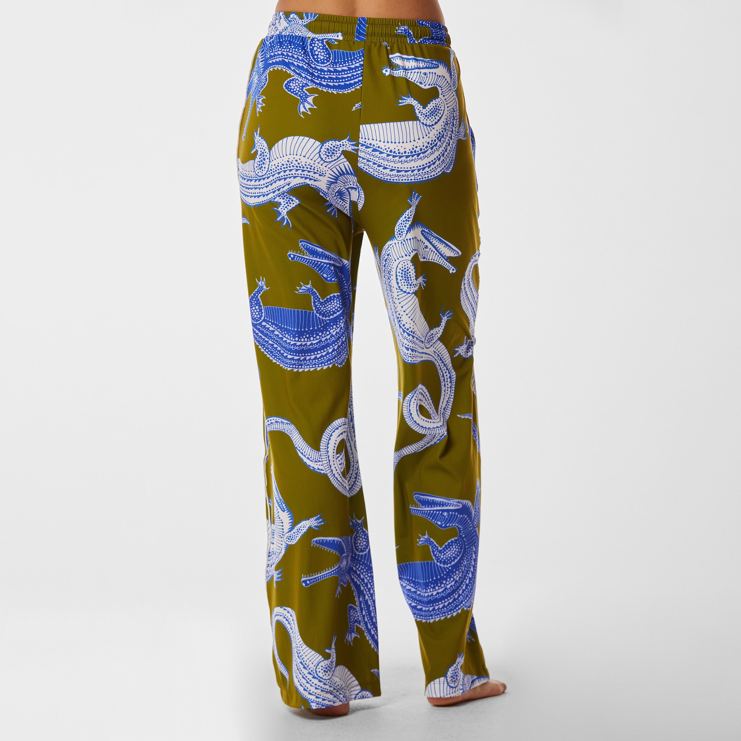 Rear view of woman wearing breathable, relaxed and buttery smooth pajama pant featuring high-waist cut, side pockets, front tie and stunning Nile gator print.