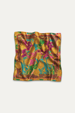 The Printed Satin Scarf - Dolce Sun features an ornate gold baroque sun medallion on green, magenta, and teal satin. Its shiny, slightly wrinkled finish adds luxury, making it a standout accessory against a white backdrop.