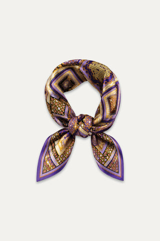 The Printed Satin Scarf - Riviera Chain features a knotted center and an elegant geometric and abstract pattern in gold, brown, and purple tones with a purple border, beautifully displayed on a white background.