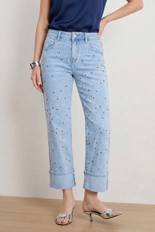 A person in Ren Cropped Cuff Jean - Confetti, a navy sleeveless top, silver bracelet, and silver heeled sandals stands indoors against a plain wall.