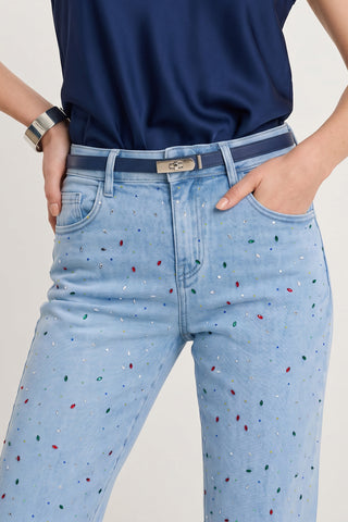 Wearing the Ren Cropped Cuff Jean - Confetti, crystal embellished with colorful sequins, paired with a metallic belt, navy blue top, and silver cuff bracelet, one hand tucked in the pocket.