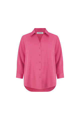 The Sara Silk Blouse - Petal Pink is a bright pink, long-sleeve silk blouse with a collar, relaxed fit, and high-low hem, shown against a plain white background.