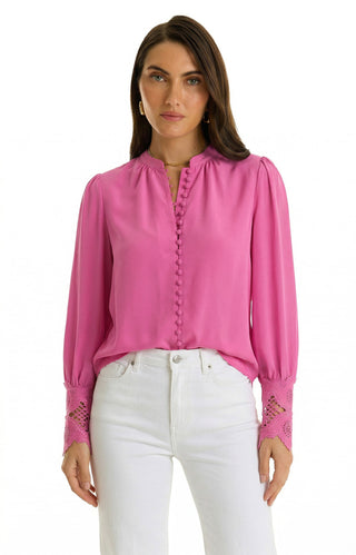 A woman stands against a white background wearing the Blake Lace Sleeve Blouse in Petal Pink, featuring fabric-covered buttons and lace-detailed cuffs, paired with high-waisted white jeans.