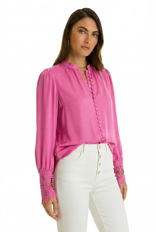A woman wears the Blake Lace Sleeve Blouse in Petal Pink, featuring lace cuff details and fabric-covered buttons, paired with high-waisted white pants. She stands facing forward against a plain white background.