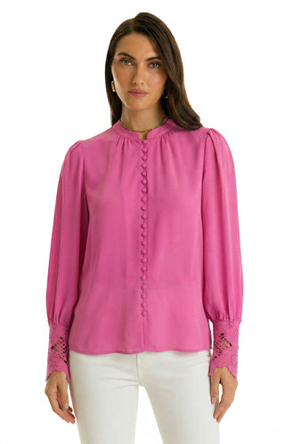 A woman wears the Blake Lace Sleeve Blouse in Petal Pink, featuring button details and lace cuffs, paired with white pants. She stands facing forward against a plain white background.