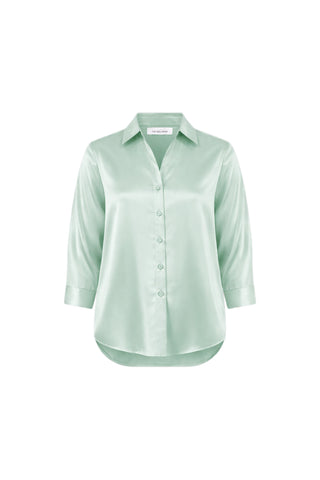 The Sara Silk Blouse - Mint is a light green, long-sleeve silk blouse with a collar and button-down front, crafted from silky fabric. It features a slightly curved hem and relaxed fit, shown on a white background.