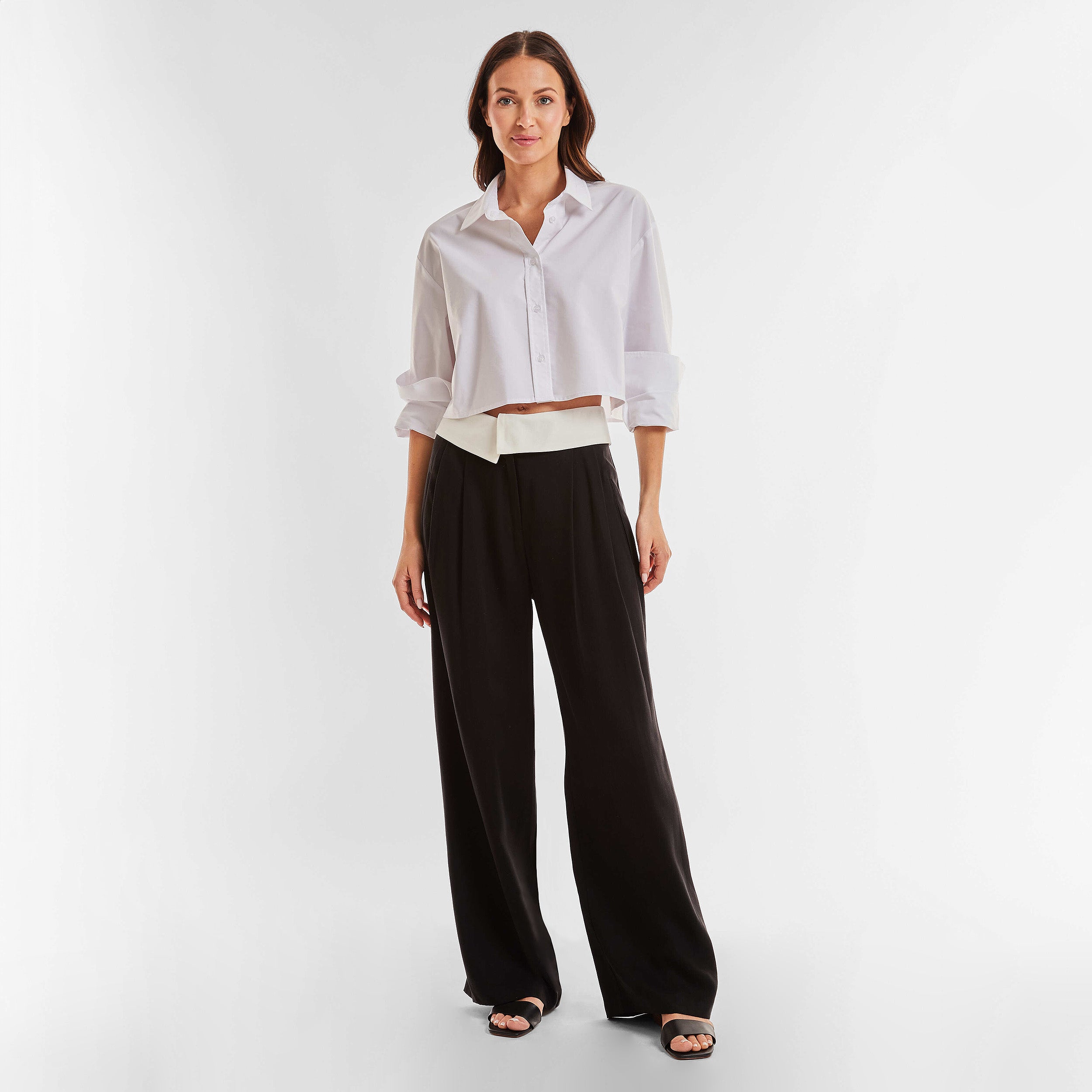 Full view of woman wearing black trousers with white foldover waistband detail.