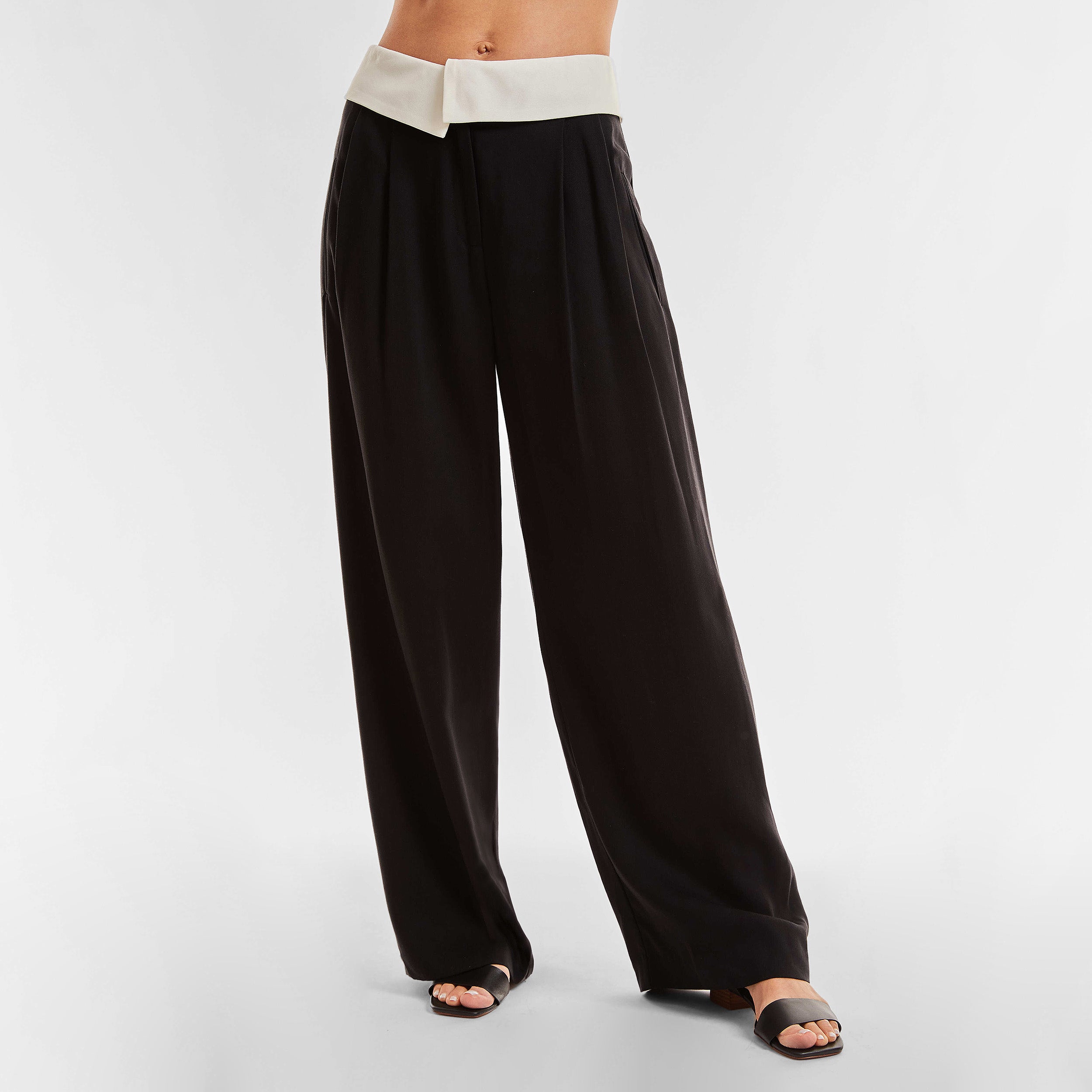 Front view of woman wearing black trousers with white foldover waistband detail.