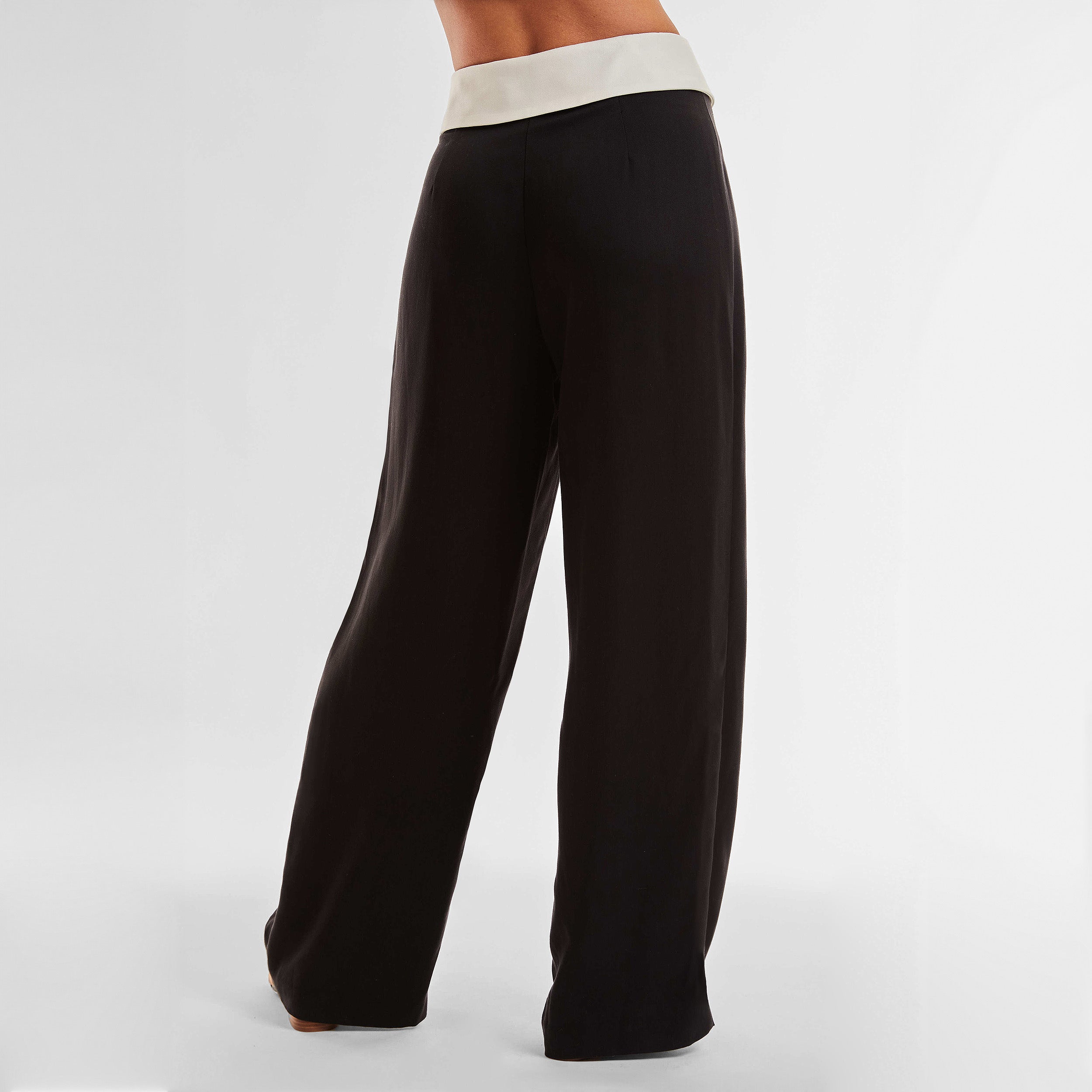 Rear view of woman wearing black trousers with white foldover waistband detail.